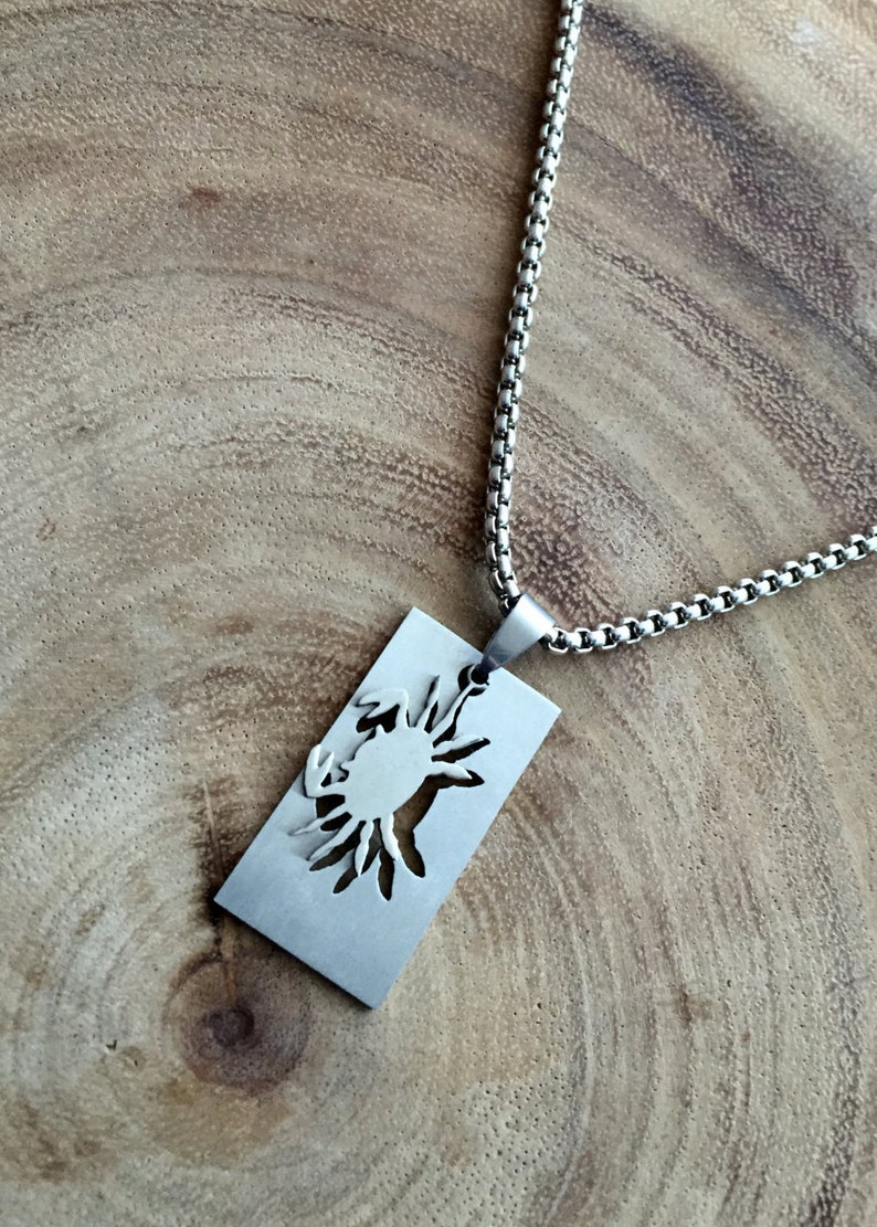 May include: A silver chain necklace with a rectangular pendant featuring a cutout design of a crab.