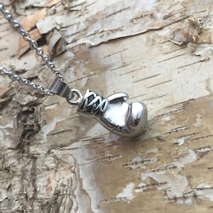 May include: A silver boxing glove pendant necklace. The pendant is detailed with a black strap and laces. The necklace is on a silver chain.