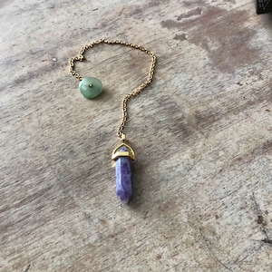 May include: A gold chain necklace with a purple crystal pendant and a green stone charm.