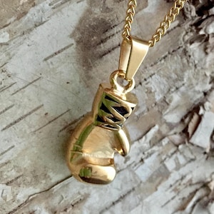 May include: A gold-tone boxing glove pendant necklace. The pendant is detailed with black accents and hangs from a gold chain.