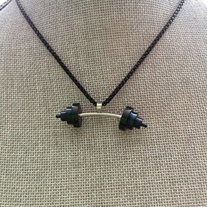 May include: A black chain necklace with a black barbell pendant. The barbell is made of stacked black squares.