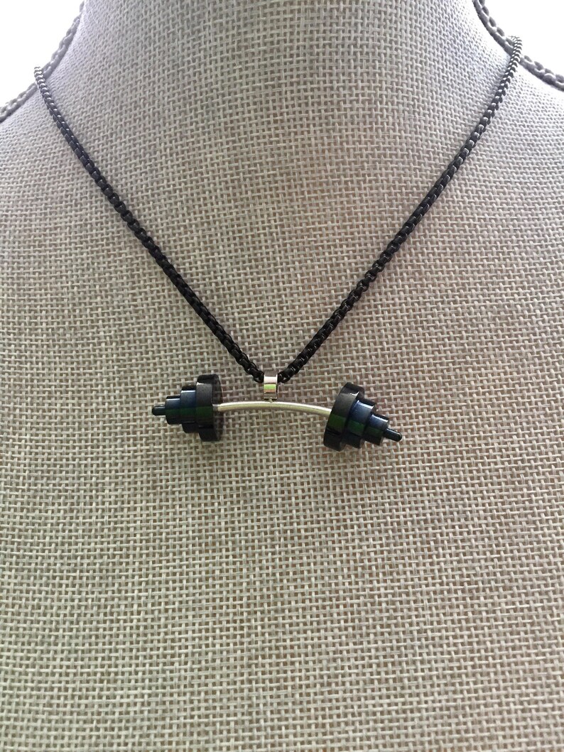 May include: A black chain necklace with a black barbell pendant. The barbell is made of stacked black squares.