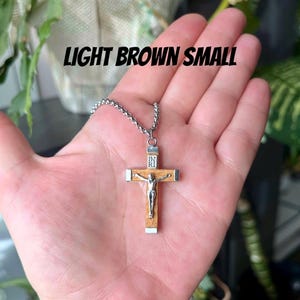 May include: A light brown wooden cross necklace with a silver chain and a silver Jesus figure on the cross. The cross is small and the chain is about 18 inches long.