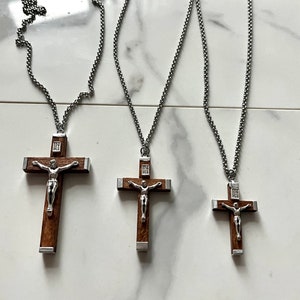 May include: Three silver chains with wooden crucifix pendants. The crucifixes have a silver figure of Jesus on a brown wooden cross. The chains are of varying lengths.