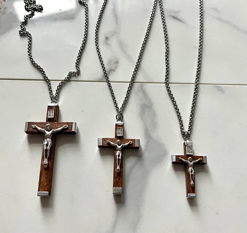 May include: Three silver chains with wooden crucifix pendants. The crucifixes have a silver figure of Jesus on a brown wooden cross. The chains are of varying lengths.