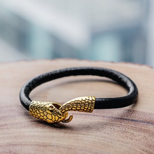 May include: A black leather bracelet with a gold snake head clasp.