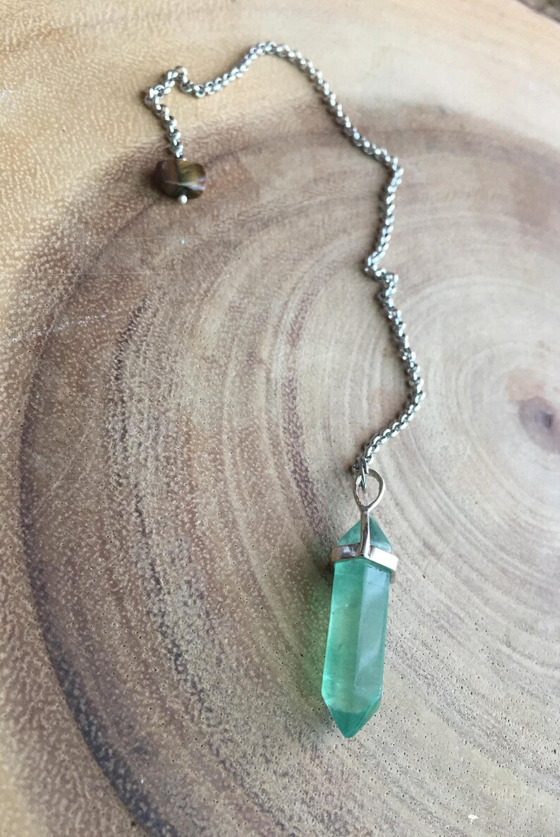 May include: A green crystal pendulum with a silver chain and a brown tiger's eye stone at the top.