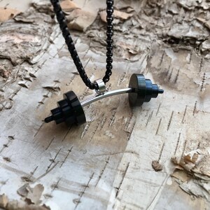 May include: A black barbell necklace with a silver chain. The barbell is made of stacked black rings and a silver bar.