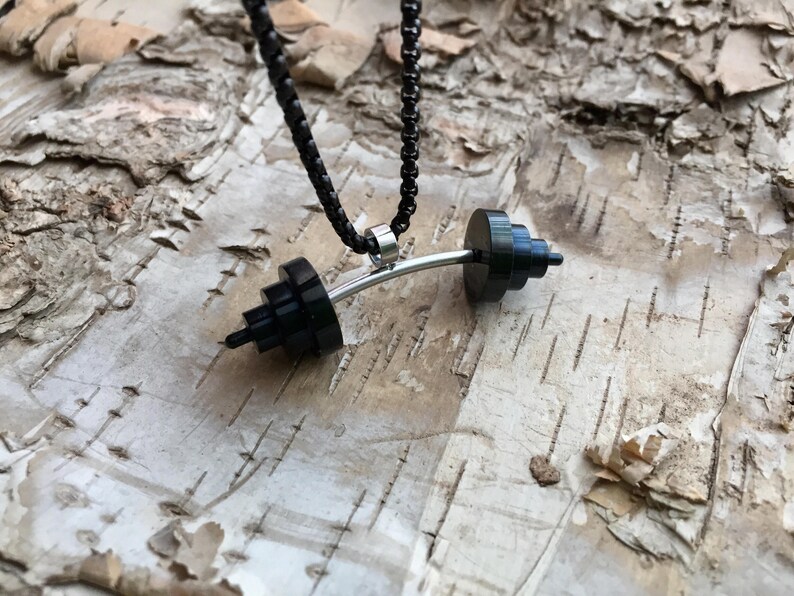 May include: A black barbell necklace with a silver chain. The barbell is made of stacked black rings and a silver bar.