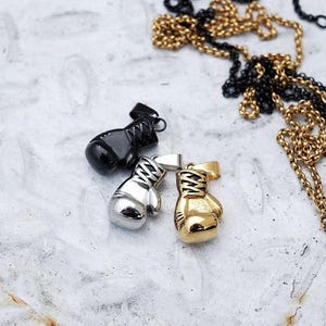 May include: Three silver and gold boxing glove pendants. The pendants are on a white surface.