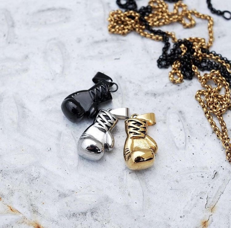 May include: Three silver and gold boxing glove pendants. The pendants are on a white surface.