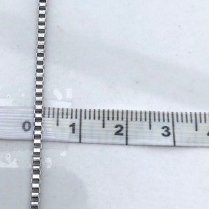 May include: A silver chain necklace measuring 5 cm in length. The chain is made of small, square links.