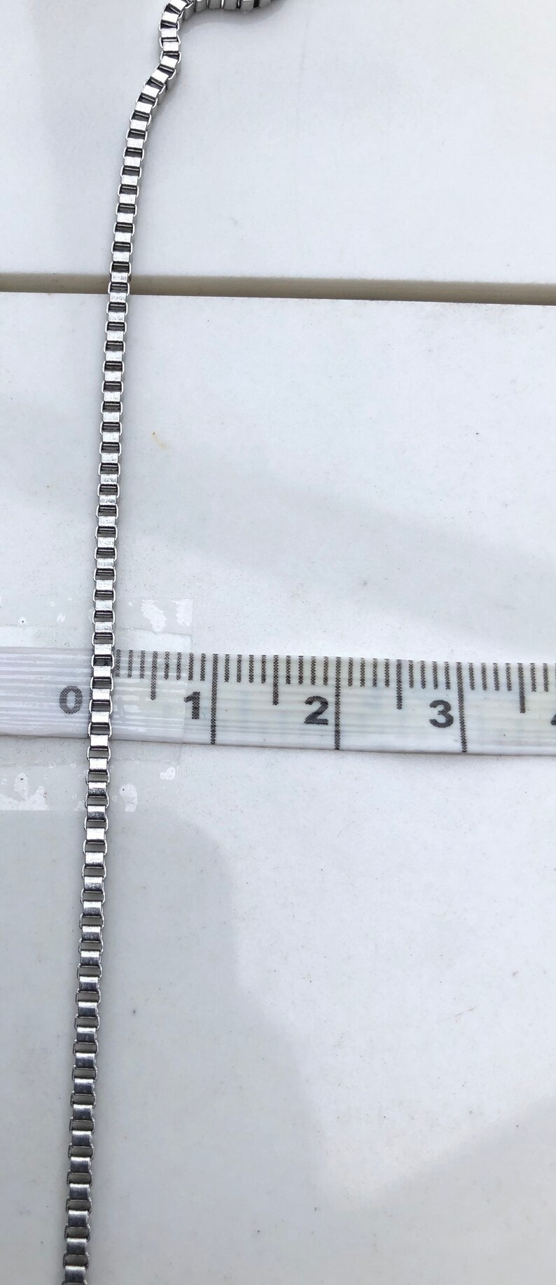 May include: A silver chain necklace measuring 5 cm in length. The chain is made of small, square links.