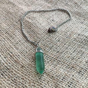 May include: A silver chain necklace with a green crystal pendant. The pendant is a point and has a silver cap at the top.