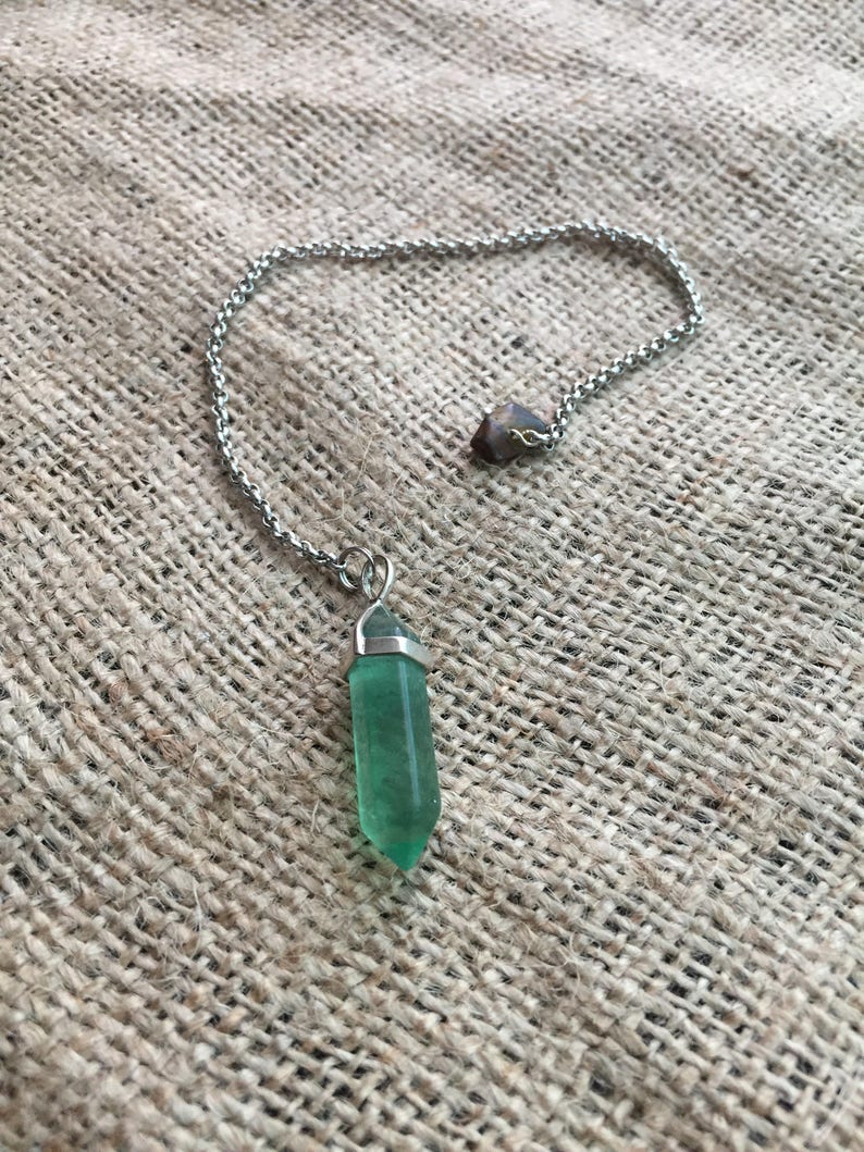 May include: A silver chain necklace with a green crystal pendant. The pendant is a point and has a silver cap at the top.