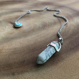 May include: A silver chain necklace with a white and gray crystal pendant and a blue evil eye charm.