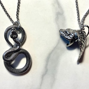 以下が含まれることがあります： 銀製の蛇のネックレスが2本。1本のネックレスは、巻き付いた蛇のペンダントが付いており、もう1本は、口を開けた蛇の頭のペンダントが付いています。