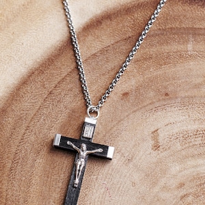 May include: A silver chain necklace with a black wooden crucifix pendant. The crucifix features a silver figure of Jesus Christ and the inscription "INRI" on the top.