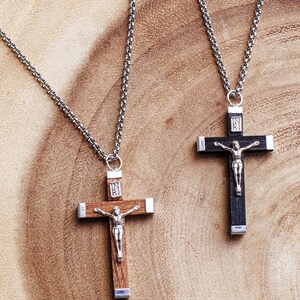 May include: Two silver chains with wooden crucifix pendants. The crucifixes are both dark wood with silver accents and the inscription "INRI" on the front. One crucifix is brown wood and the other is black wood.