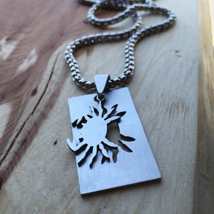 May include: A silver chain necklace with a rectangular pendant featuring a cut-out sun design.