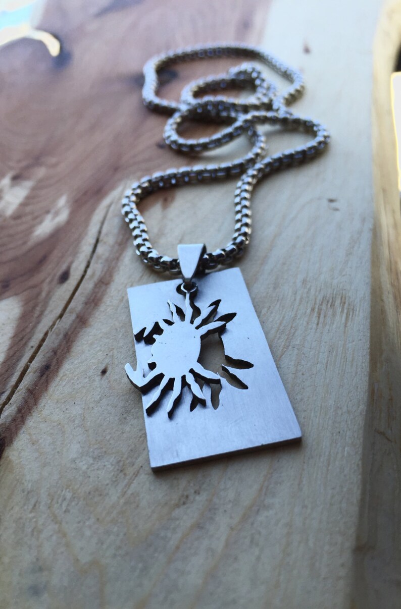May include: A silver chain necklace with a rectangular pendant featuring a cut-out sun design.