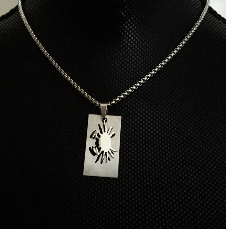 May include: A silver chain necklace with a pendant featuring a cutout design of a crab. The pendant is rectangular and hangs from a silver chain.