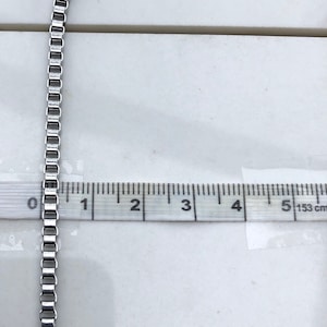 May include: A silver chain necklace measuring 5 inches long. The chain is made of small, square links.