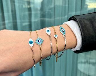 Può includere: Cinque braccialetti a catena dorati e argentati con ciondoli a forma di occhio turco blu e bianco. I ciondoli hanno forme diverse, tra cui un fiore, un ovale e una lacrima.
