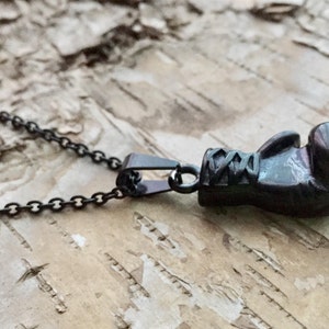 May include: A black chain necklace with a black boxing glove pendant. The pendant is detailed with stitching and laces.