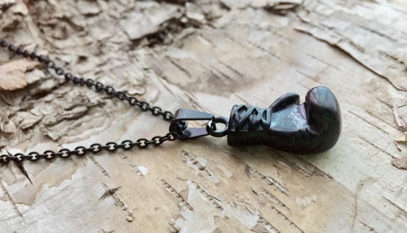 May include: A black chain necklace with a black boxing glove pendant. The pendant is detailed with stitching and laces.