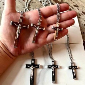 May include: Five silver chain necklaces with wooden crucifix pendants. The crucifixes are different sizes and have a silver Jesus figure on them. Some of the crucifixes are brown wood and some are black wood.
