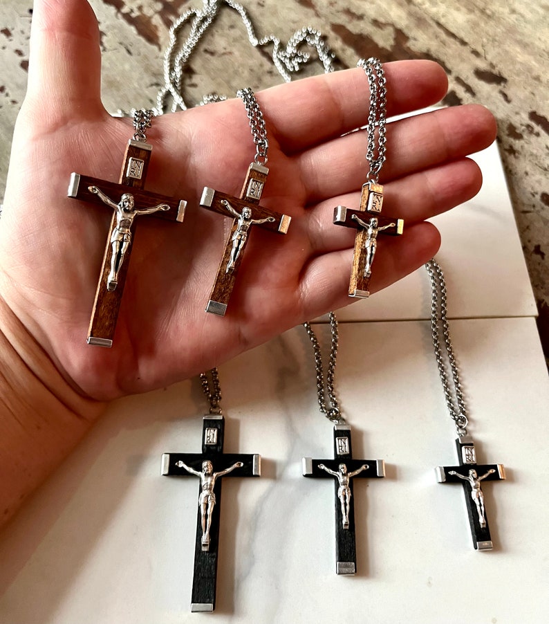 May include: Five silver chain necklaces with wooden crucifix pendants. The crucifixes are different sizes and have a silver Jesus figure on them. Some of the crucifixes are brown wood and some are black wood.
