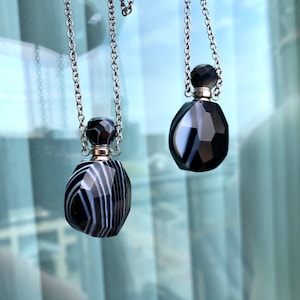 Peut inclure: Deux colliers avec pendentifs en agate noire et blanche et chaînes argentées. Les pendentifs ont la forme de flacons avec un design facetté.