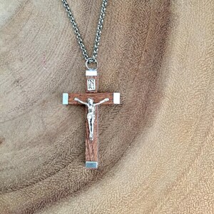 May include: A wooden crucifix necklace with a silver chain and a silver figure of Jesus Christ. The crucifix has a silver plaque with the inscription "INRI" on the top.