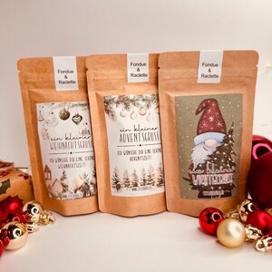 May include: Three brown paper pouches labelled "Fondue & Raclette" with festive designs. One features a gnome with a Christmas tree, another has a winter village scene, and the third displays a forest. Each pouch has German text.