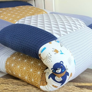 Könnte beinhalten: Ein blaues und gelbes Patchwork-Bodenkissen mit einem weißen Stoffpanel, auf dem ein Comic-Bär mit einem blauen Bandana abgebildet ist. Das Kissen besteht aus verschiedenen gemusterten Stoffen, darunter Streifen, geometrische Muster und ein weißer Stoff mit einem blauen und gelben Blumendesign.