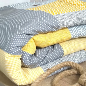 Könnte beinhalten: Eine gelbe und graue Patchwork-Decke mit einem Seil darum gebunden. Die Decke besteht aus verschiedenen Stoffen mit verschiedenen Mustern, darunter Sterne, Rauten und Zickzack.