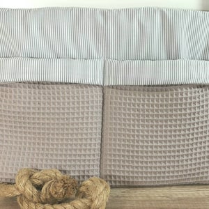 Op de afbeelding: Een beige opbergzak van geweven stof met twee vakken en een wit-grijze gestreepte voering. De zak heeft aan elke kant een handvat en hangt aan een houten oppervlak.