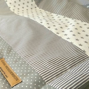 Könnte beinhalten: Eine graue und weiße Patchwork-Babydecke mit einem Etikett mit der Aufschrift "Lotta Holgerson, designed for you".
