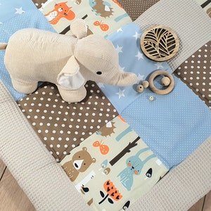 May include: A beige plush elephant toy on a multi-colored patchwork play mat with brown and blue squares. The mat has a variety of patterns including polka dots, stars, and woodland animals.