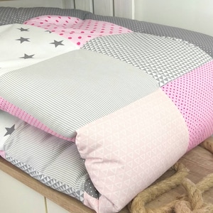 May include: A pink and gray patchwork baby quilt with a variety of patterns, including stars, polka dots, and triangles.