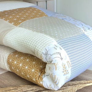 Könnte beinhalten: Eine Patchwork-Decke mit verschiedenen geometrischen und floralen Mustern in Beige-, Braun-, Weiß- und Blautönen. Die Decke ist in der Mitte gefaltet und zeigt auf einer Seite ein Hasenmotiv.