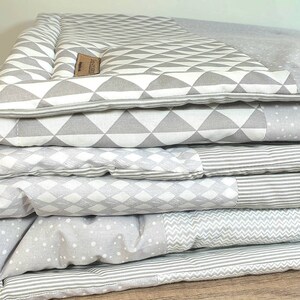 Könnte beinhalten: Ein Stapel aus vier grauen und weißen Babydecken mit Mustern. Die oberste Decke hat ein geometrisches Muster aus Dreiecken, die zweite Decke hat ein Rautenmuster, die dritte Decke hat ein kleines weißes Punktmuster und die unterste Decke hat ein Zickzackmuster.