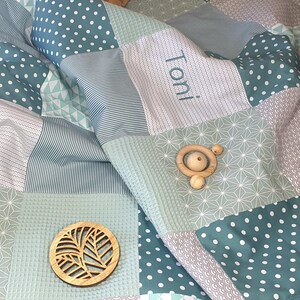 May include: A green and white patchwork baby blanket with the name "Toni" embroidered on it. The blanket is made of different fabrics with various patterns, including polka dots, stripes, and geometric designs.