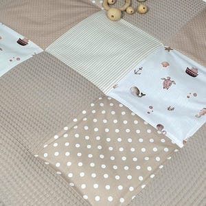 Könnte beinhalten: Eine beige und weiße Patchwork-Spielmatte mit verschiedenen Mustern, darunter Punkte, Streifen und ein nautisches Thema. Die Matte ist aus weichem, bequemem Stoff gefertigt und perfekt für Babys und Kleinkinder.
