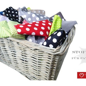 Può includere: Un cesto di vimini bianco pieno di quadrati di stoffa colorati per patchwork. I quadrati di stoffa hanno pois, stelle e motivi a scacchi. Il cesto è etichettato con "Stoffpaket für Patchwork" e "Lotta-Holgerson designed for you".