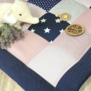 Könnte beinhalten: Eine marineblaue und rosafarbene Patchwork-Spielmatte mit weißen Sternen und Punkten. Die Matte zeigt ein Stofftier-Elefant, ein Holz-Ornament in Blattform und einen Holz-Beißring.
