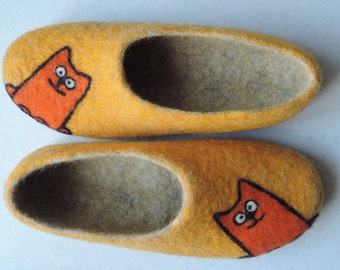 May include: A pair of yellow felt slippers with orange cat designs. The slippers have a soft, fuzzy interior.