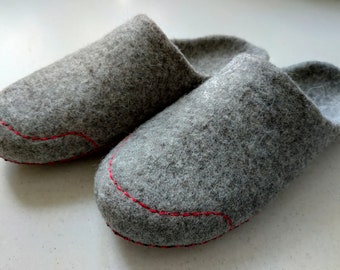 May include: A pair of gray felt slippers with red stitching around the edges.