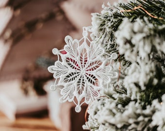 May include: A white crocheted snowflake ornament hanging on a snowy artificial Christmas tree.